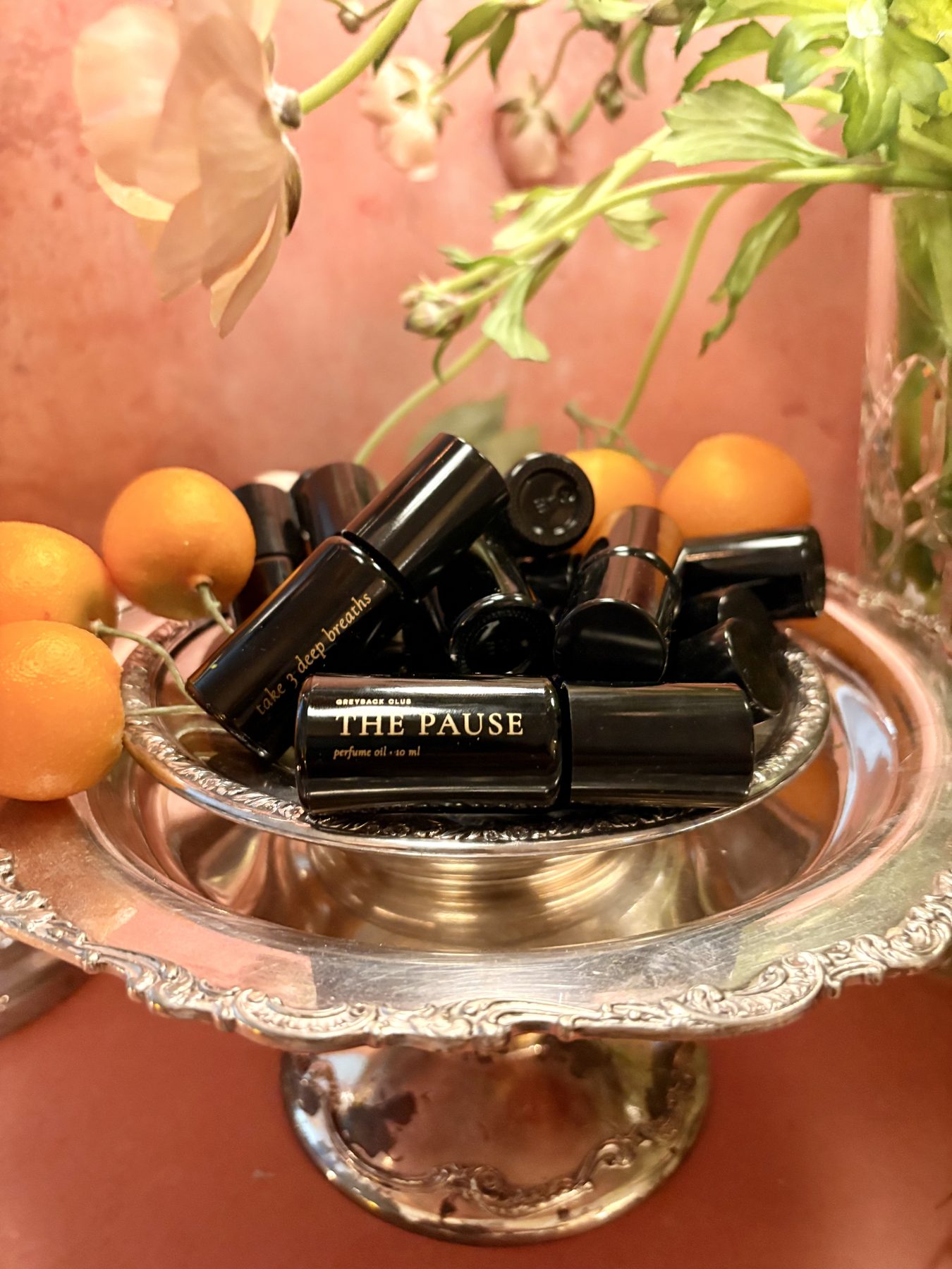 Bottles of The Pause piled on a silver tray with kumquats and flowers